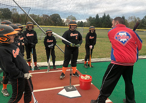 A group of people in baseball uniforms practicing batting.